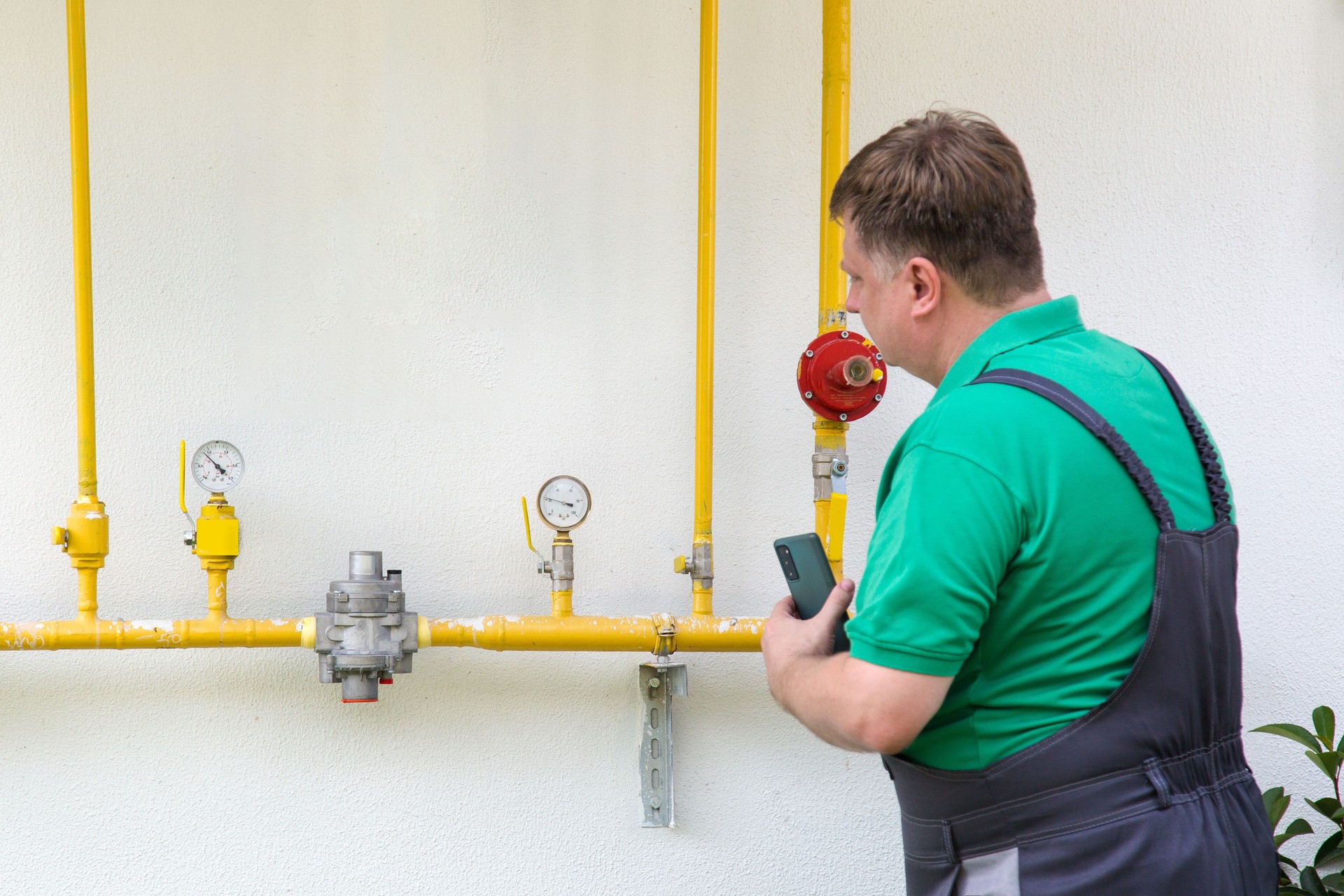 A man in work clothes looks and takes photographs of water and gas consumption meters on a smartphone